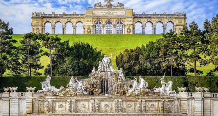 Fontaine ornée et bâtiment sur colline avec statues.