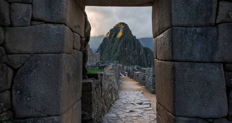 Machu Picchu through a stone doorway with distant mountain.