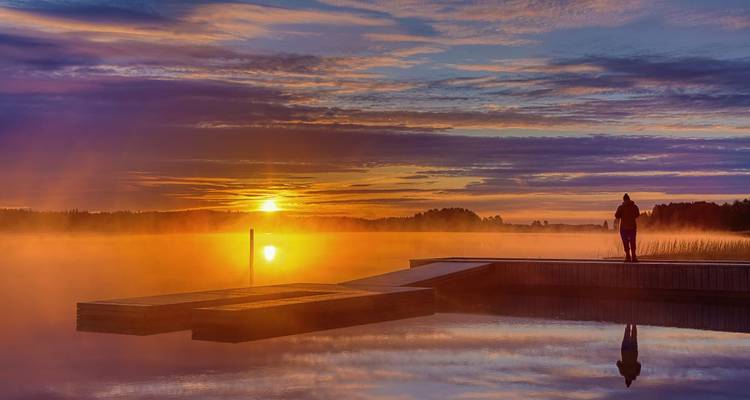 Personne debout sur un quai regardant un lever de soleil coloré au-dessus d'un lac.
