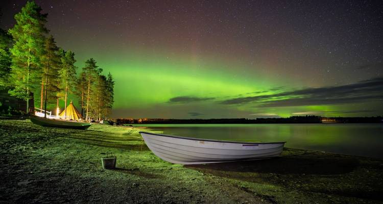 Aurores boréales au-dessus d'un bateau sur le rivage d'un lac la nuit.