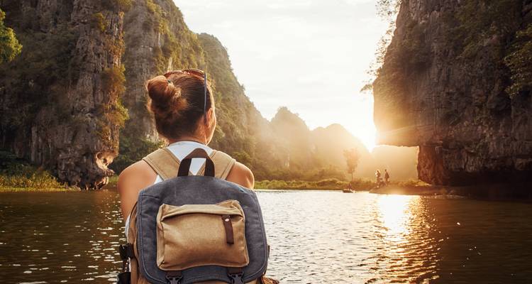 Vrouw met een rugzak kijkend naar een rotsachtig landschap bij zonsondergang.