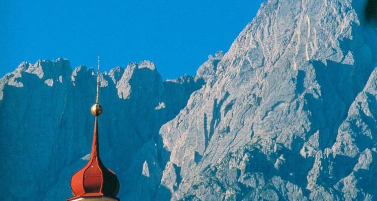 Ein Kirchturm mit einer bergigen Kulisse unter einem klaren Himmel.