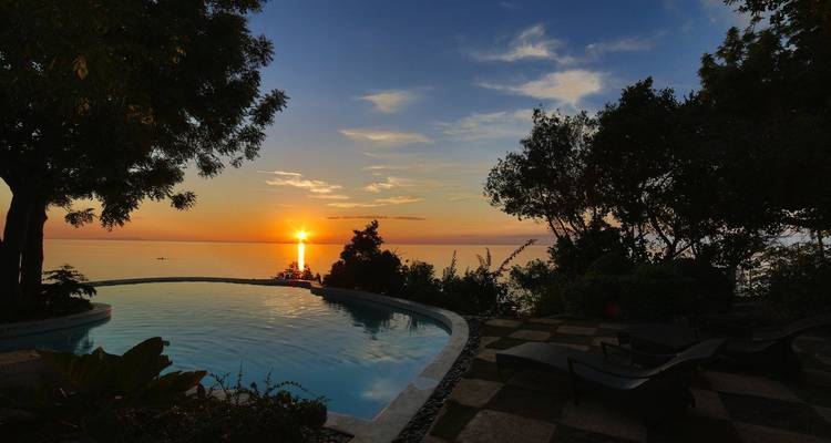 Piscine à débordement sérène surplombant la mer au coucher du soleil avec le soleil se couchant à l'horizon.