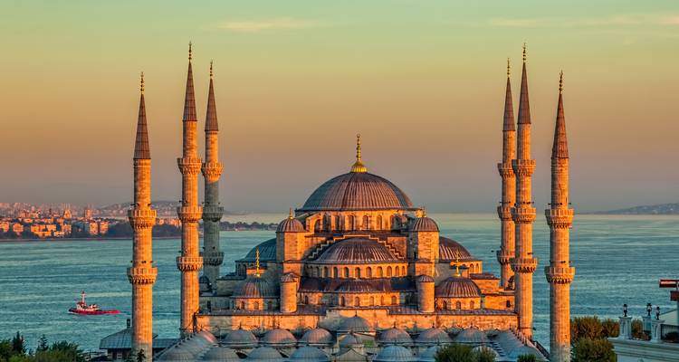De Blauwe Moskee in Istanbul met minaretten bij zonsondergang, met de Bosporus op de achtergrond.