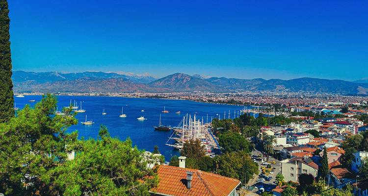 Vista panorámica de la Bahía de Fethiye con veleros y montañas distantes bajo un cielo azul vivido.