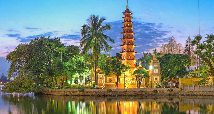 Tran Quoc Pagoda prachtig verlicht in de schemering, weerspiegeld in het rustige meer met palmbomen eromheen.