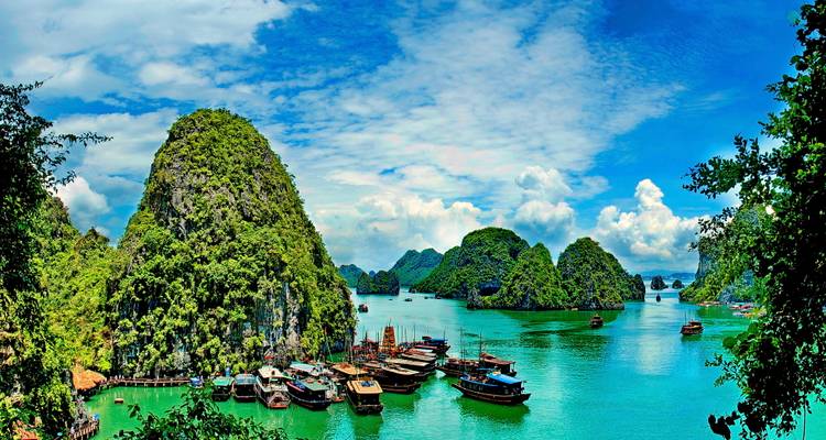 Panoramisch uitzicht op smaragdgroene wateren, kalksteeneilanden en aangemeerde jonken in Ha Long Bay onder blauwe hemels.
