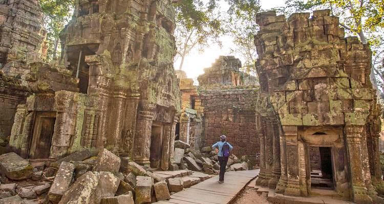 Reiziger met rugzak wandelt tussen oude, mosbegroide tempelruïnes in de Cambodjaanse jungle.