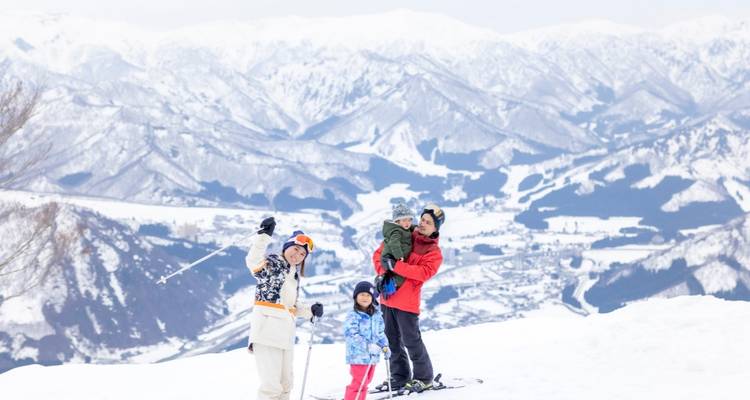 Famille faisant du ski avec des montagnes enneigées en arrière-plan.