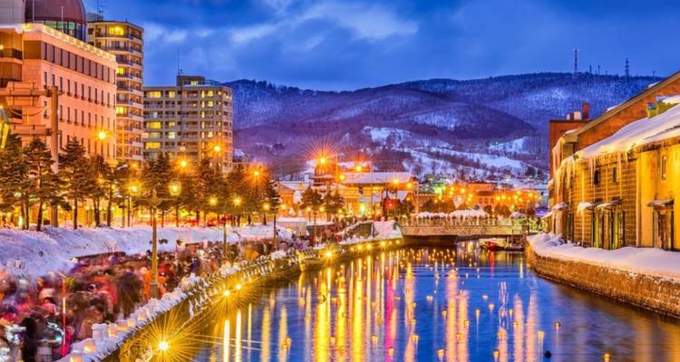 Snowy canal cityscape with warm lighting reflecting on water at night.