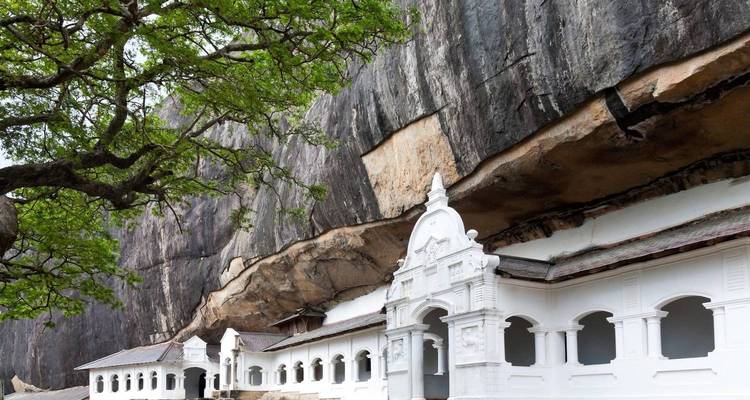 Structure de temple blanc construite contre un grand rocher.