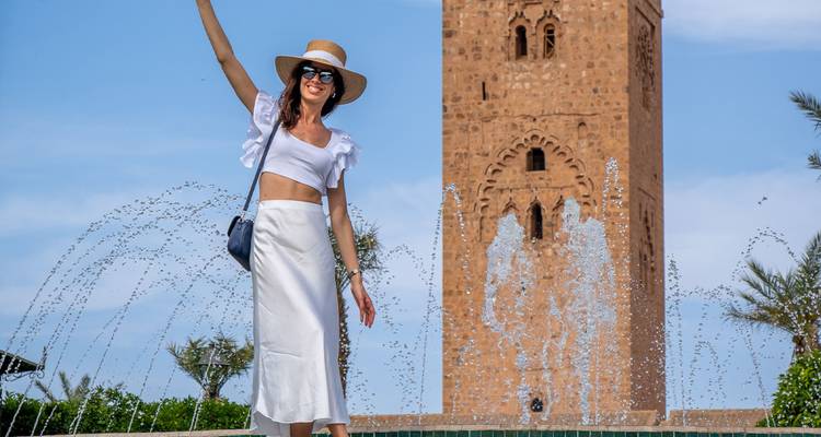 A person posing in front of a fountain with a historical tower.