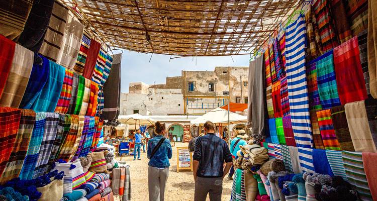Market scene with colorful textiles and people shopping.
