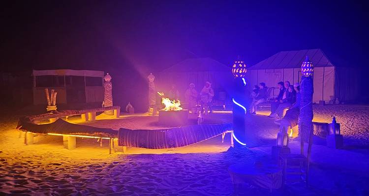 Nighttime desert camp with a central campfire surrounded by seating.