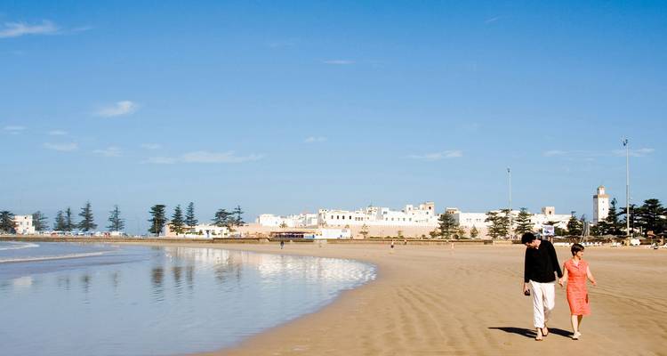 Couple walking along a sandy beach with a distant city.