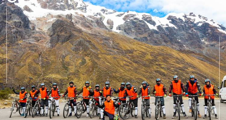 Group of cyclists posing in front of a mountain with snow-capped peaks.