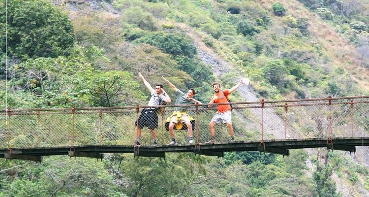 Three people posing on a suspension bridge in a mountainous area.
