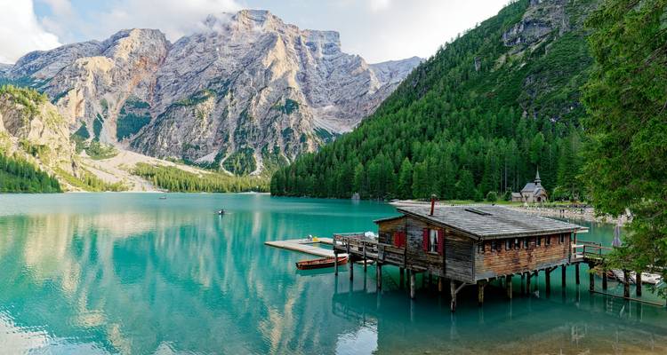 Un lac tranquille entouré de montagnes boisées avec une cabane en bois.