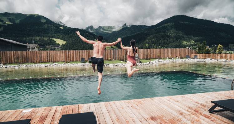 Two people jumping into a pool with mountains in the background.