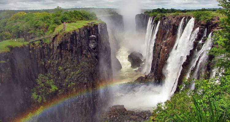 Una vista impresionante de las Cataratas Victoria con un arcoíris vibrante y vegetación exuberante.