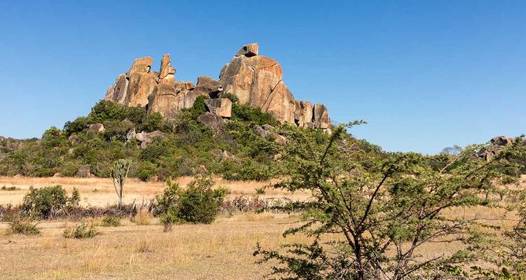 Afloramiento rocoso en una llanura seca y herbosa bajo un cielo azul despejado.