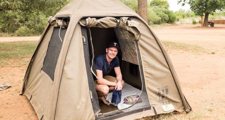 Person smiling in a tent set up in a dry camping ground.