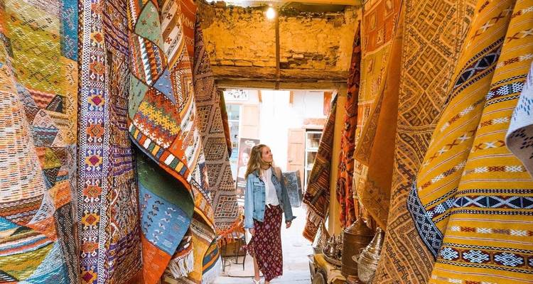 Une femme admirant des textiles marocains aux couleurs vives dans une ruelle étroite.