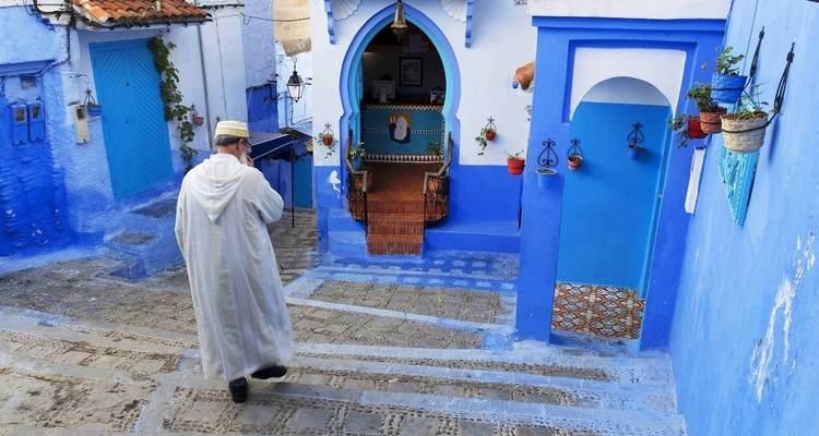 Une personne portant des vêtements traditionnels marchant dans une rue bleue à Chefchaouen.
