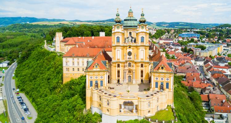 Abbaye baroque aux teintes dorées au sommet d'une colline avec vues panoramiques.