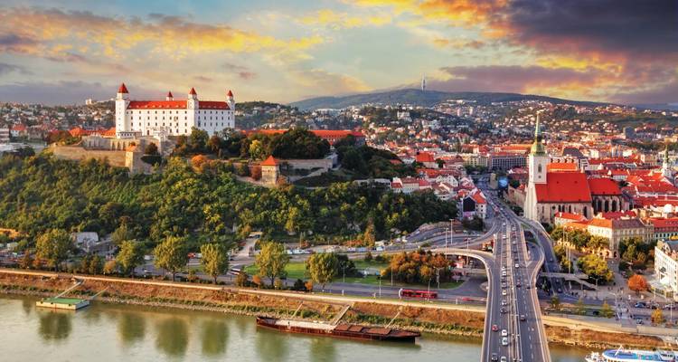 Le château de Bratislava surplombe le Danube et la ligne d'horizon de la ville sous un ciel de coucher de soleil coloré.