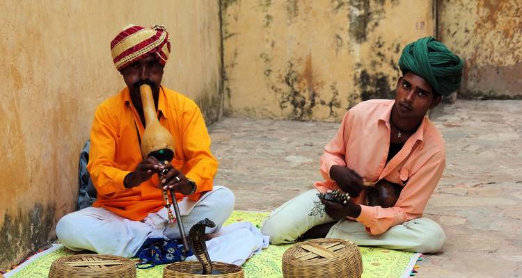 Two traditional snake charmers sitting on the ground with cobras.