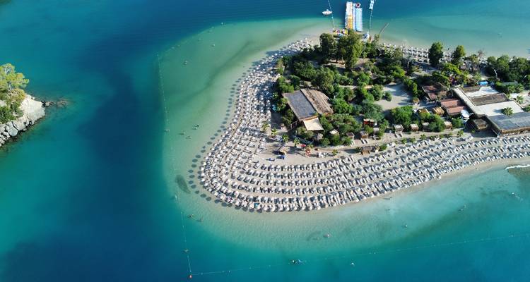 Luftaufnahme eines Strandes mit Sonnenschirmen am klaren türkisfarbenen Meer.