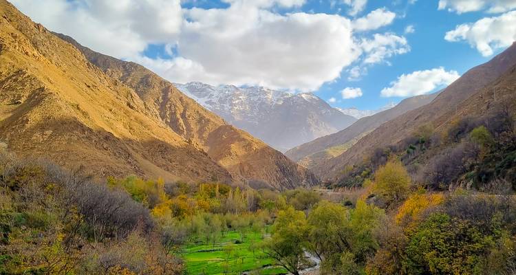 Vallée verdoyante luxuriante entourée de montagnes arides sous un ciel partiellement nuageux.