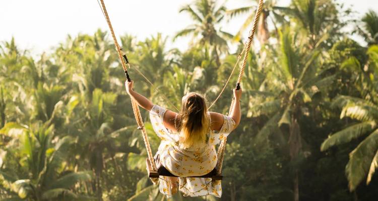 Woman on a swing with a lush tropical forest in the background.