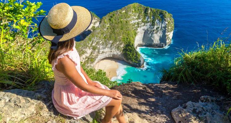 Woman sitting on a cliff overlooking a turquoise beach.