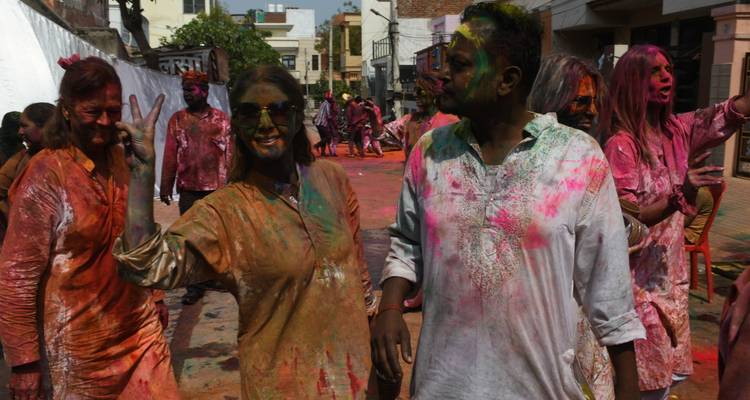 People covered in colorful powders celebrating Holi festival on a street.