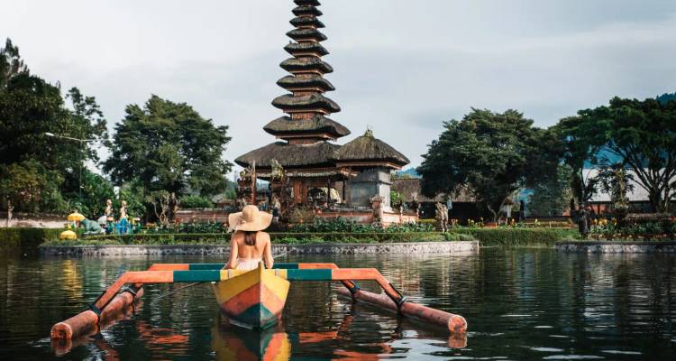 Vrouw in een boot voor een tempel omringd door water.