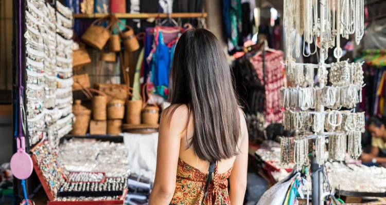Achteraanzicht van een vrouw die een markt vol met ambachtswerk en sieraden bekijkt.