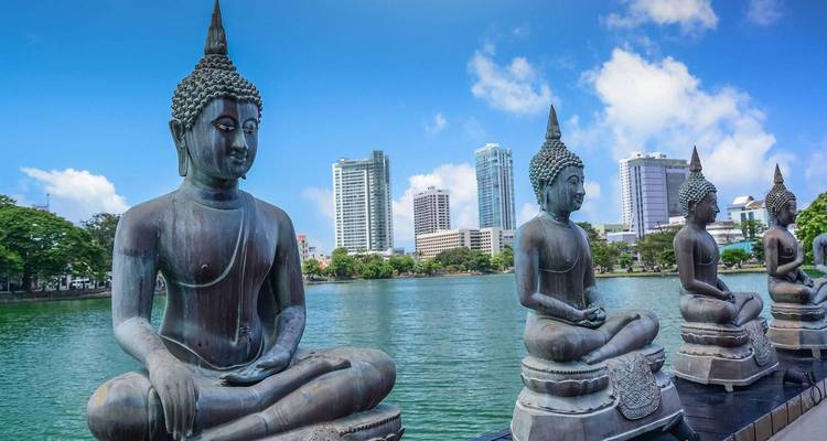 Statues de Bouddha surplombant un lac avec l'horizon urbain en arrière-plan.