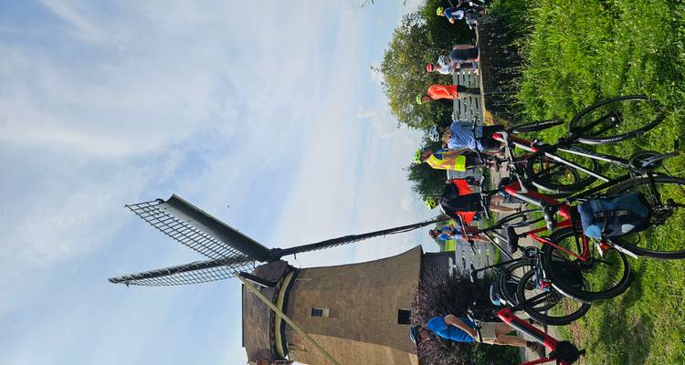 Groupe de cyclistes près d'un moulin à vent dans une zone rurale.