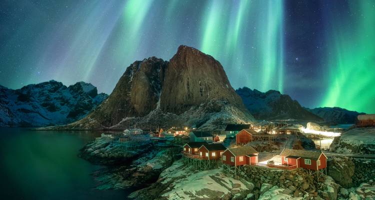 Northern lights over cabins and mountains at night.