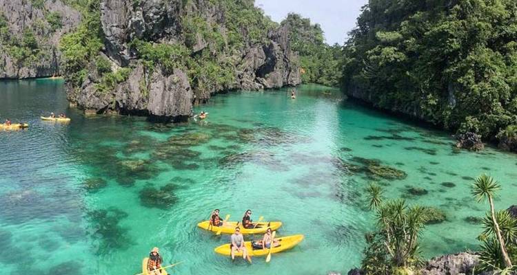 Des gens faisant du kayak dans un lagon turquoise entouré de falaises.