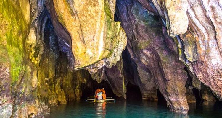Des gens dans un bateau entrant dans une grotte avec des parois rocheuses illuminées.