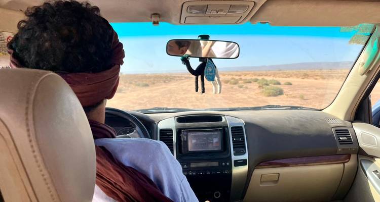Person in a car driving through a desert landscape.