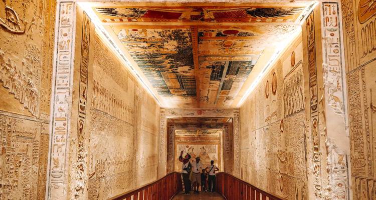 Interior of an Egyptian tomb with tourists looking at ceiling art.