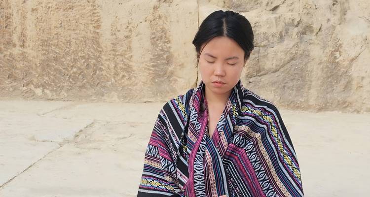 Person sitting against a sandstone background, looking contemplative.