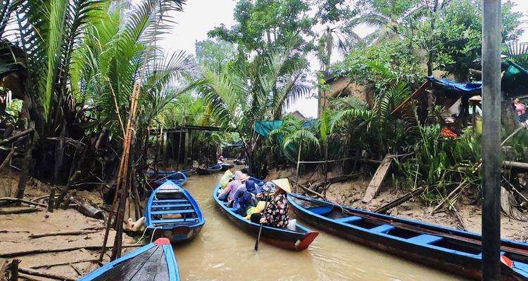Los botes de remos se deslizan por un estrecho canal bordeado de palmeras en el Delta del Mekong