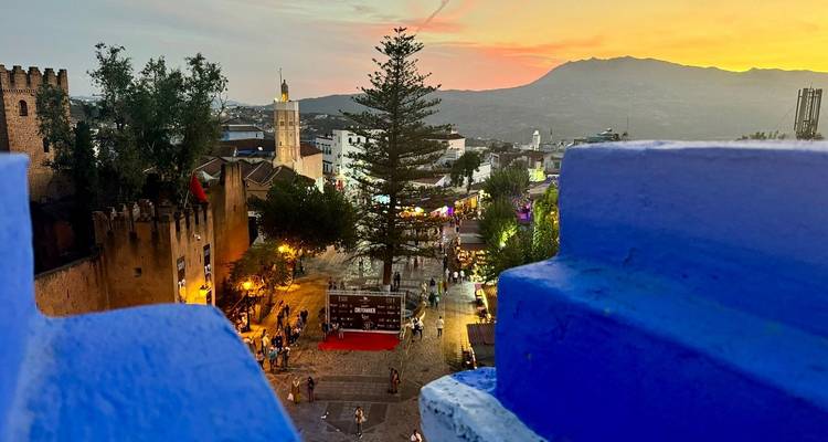 Coucher de soleil sur une ville avec une tour d'horloge visible et des montagnes.