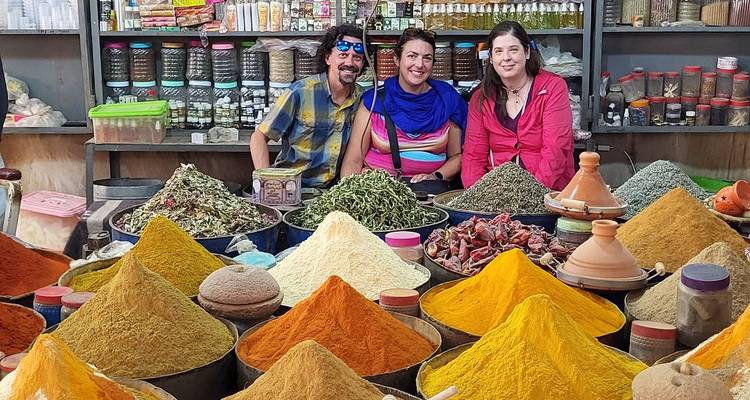 Three people in a spice market surrounded by colorful spices.