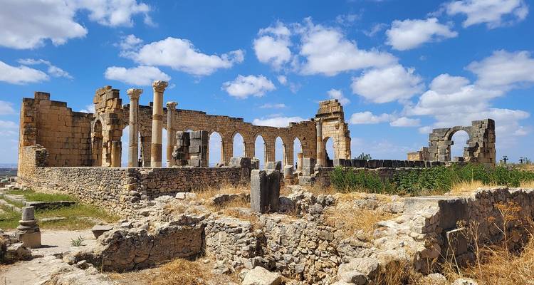 Ruines anciennes avec des arches et des colonnes sous un ciel bleu.